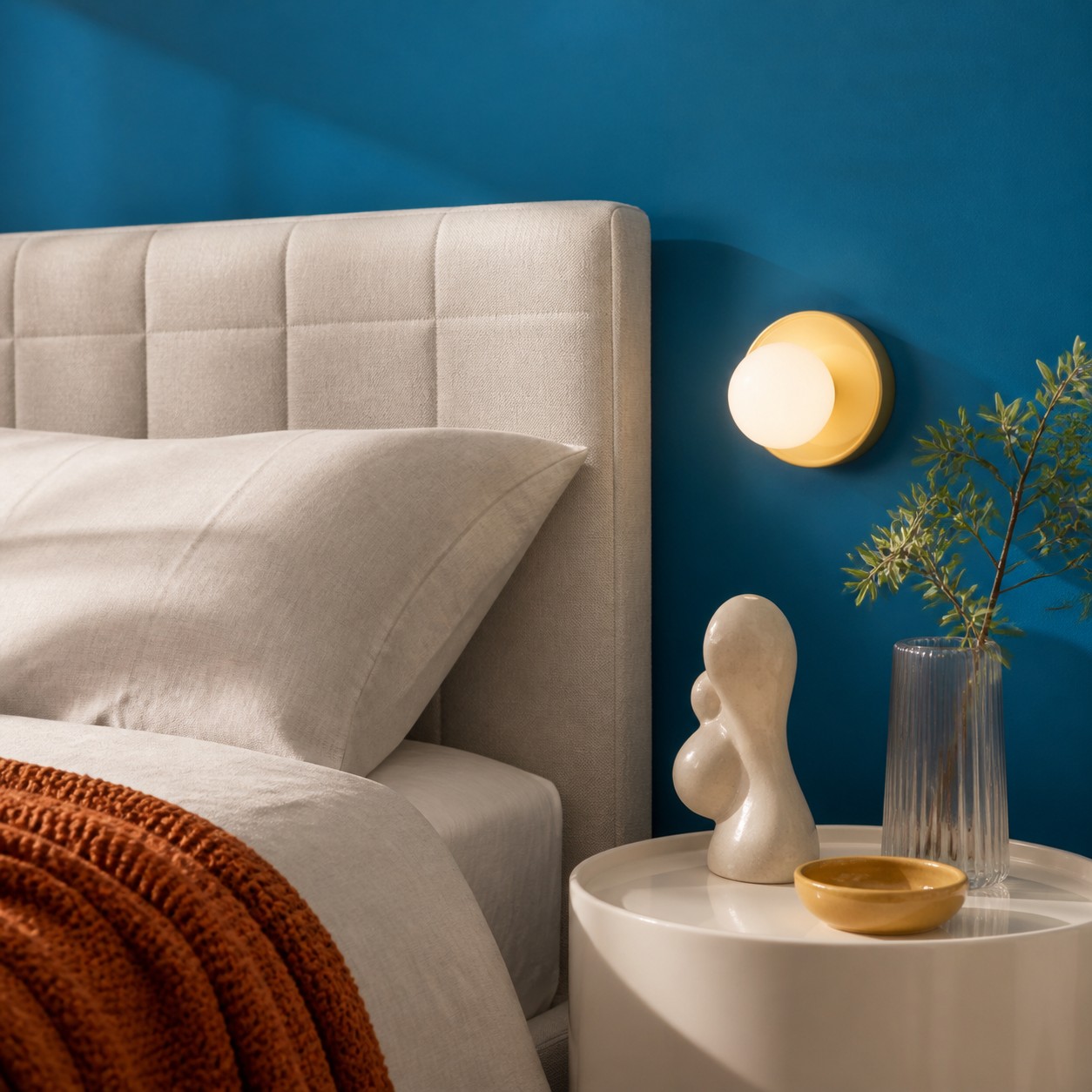 Yellow Solna wall light beside a bed on a deep blue wall