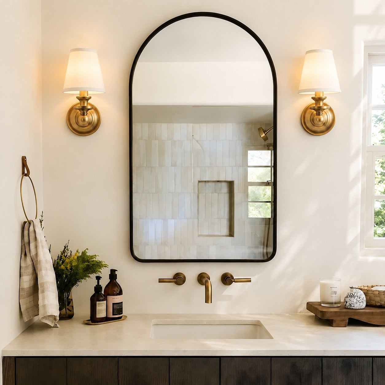 Pair of brass Kalvora wall sconces beside an arched bathroom mirror