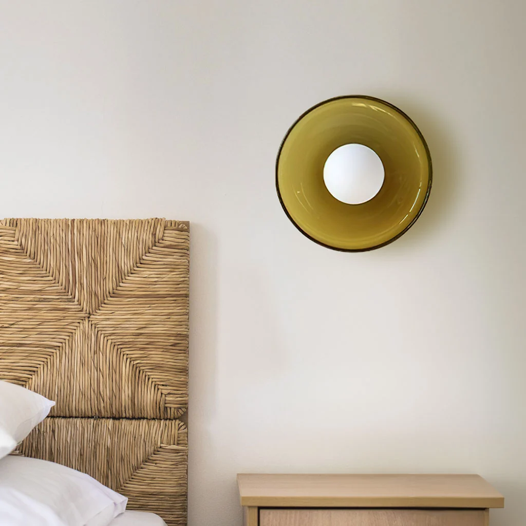 Light green glass disc wall sconce above a bed