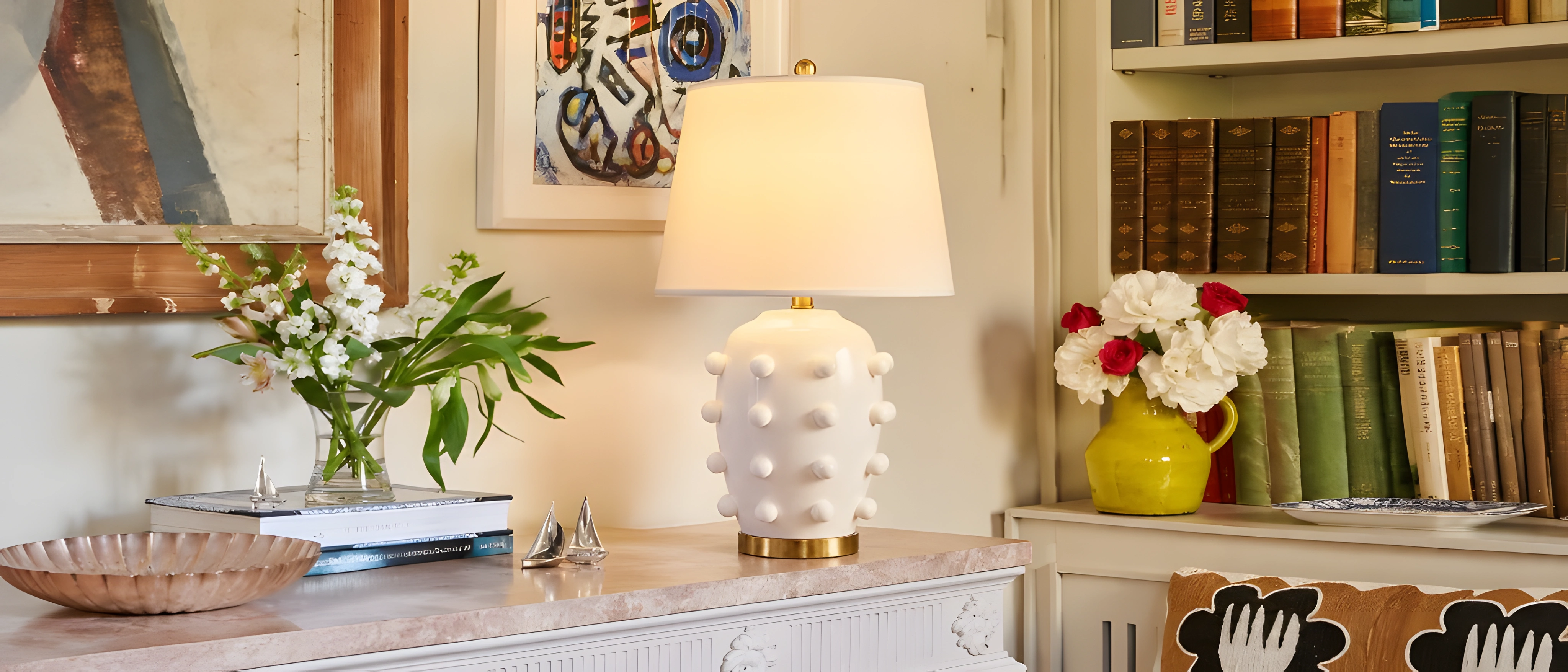 White raised-dot table lamp on a console beside a bookshelf
